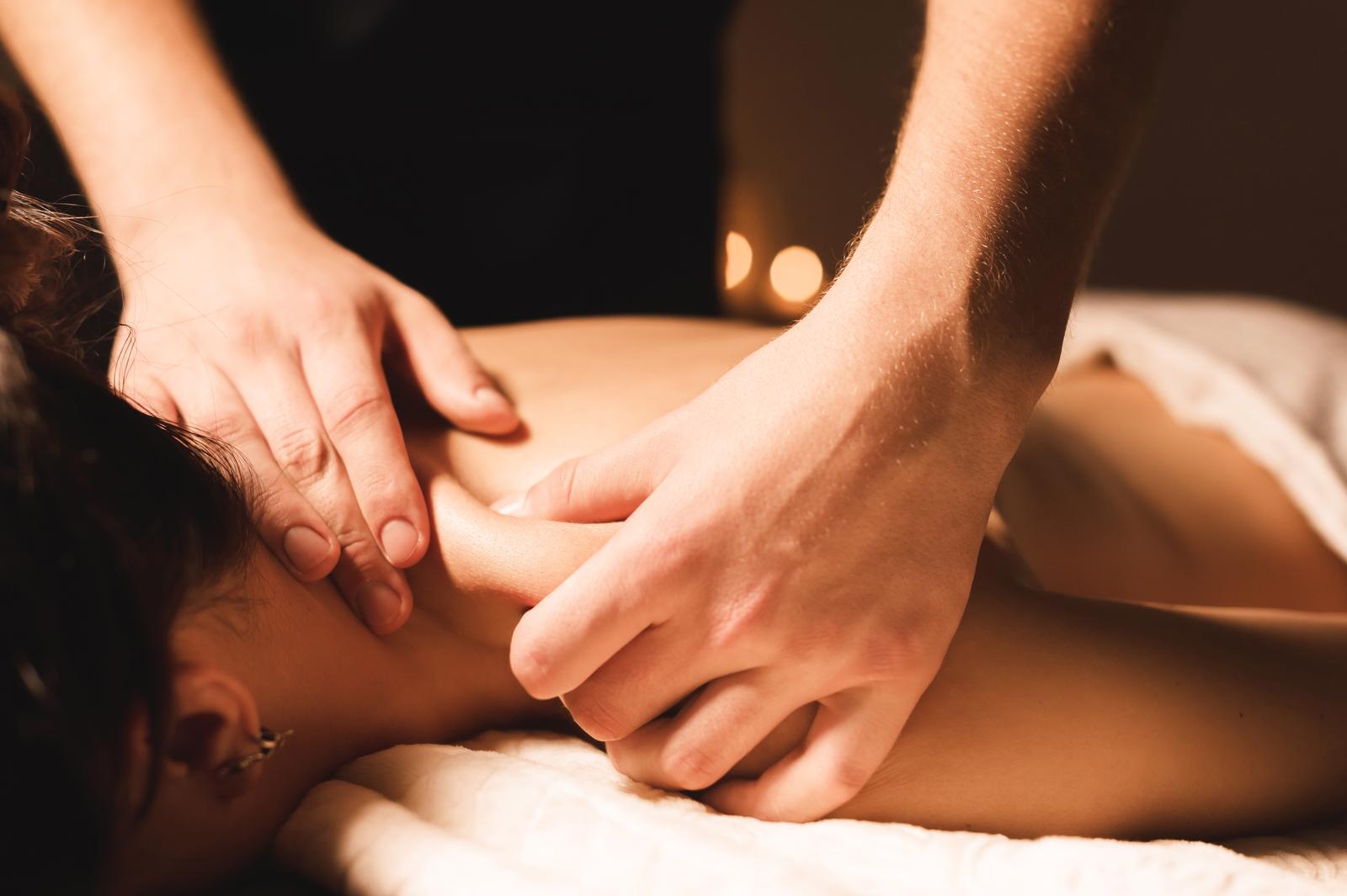Men's hands make a therapeutic neck massage for a girl lying on a massage couch in a massage spa with dark lighting. Close-up. Dark Key